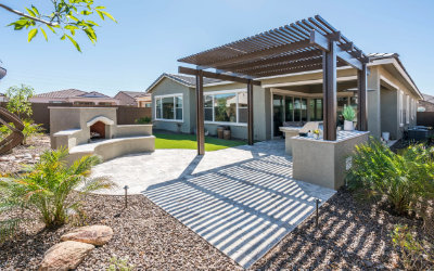 Slatted pergola shading a paved seating area beside a modern home.