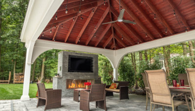 Covered pergola with a ceiling fan, fireplace and patio seating.