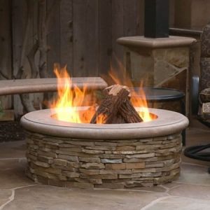 Tall stucco outdoor fireplace with a burning fire beside a paver patio.