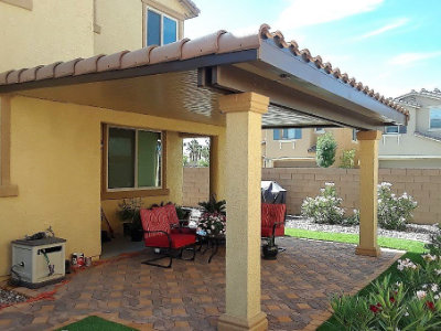 Covered backyard patio with paver flooring and patio furniture beside a stucco home.