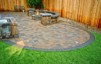 Circular paver patio with a stone fire pit set into a lawn beside a timber fence.