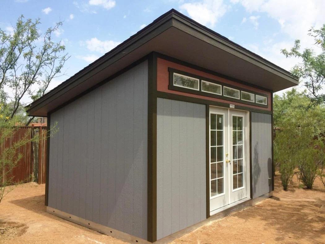 Grey backyard shed with double glass doors and a sloped roof on a gravel bed.