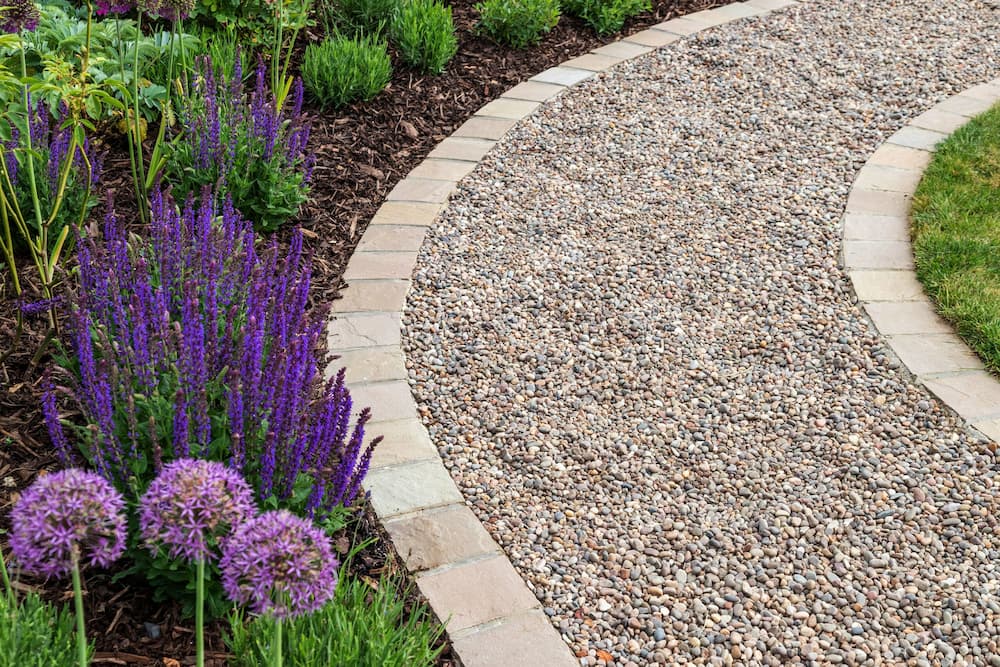 Gravel path edged with pavers curving past flowering purple and pink planting.